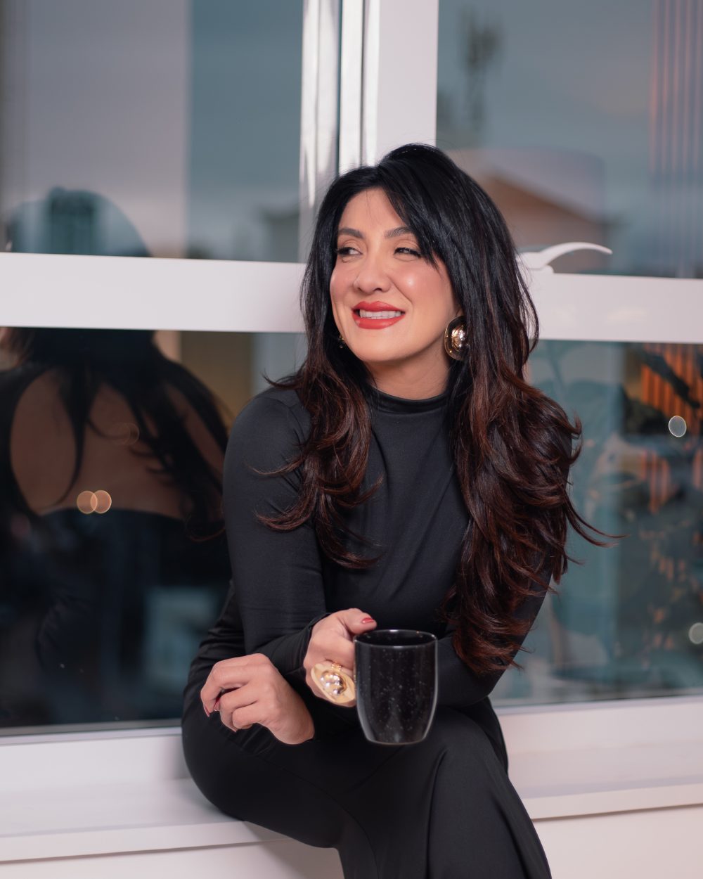 Luiziana Malheiros sorrindo, com um chá, na janela